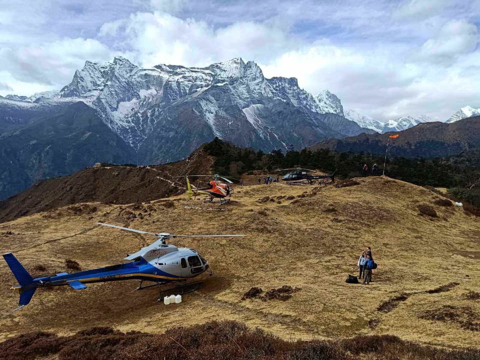 A helicopter parked on the grass ridge at Syangboche, with the snow peaks of Kongde Ri behind