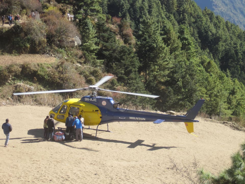 Passengers loading bags into a helicopter on a forest helipad in the Khumbu